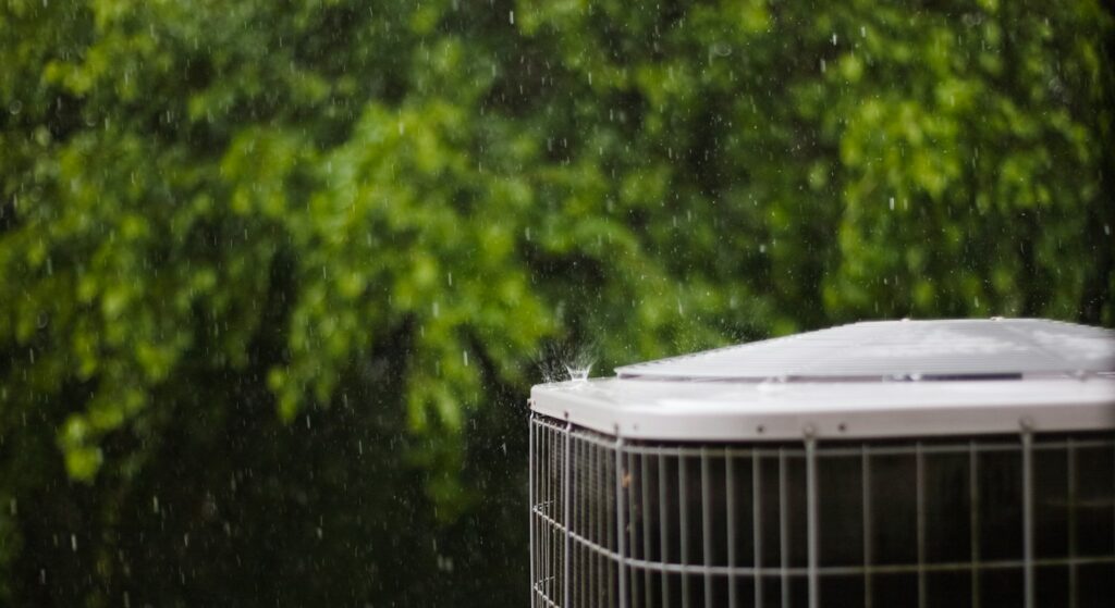 Residential air conditioner condenser unit outside a home in the rain